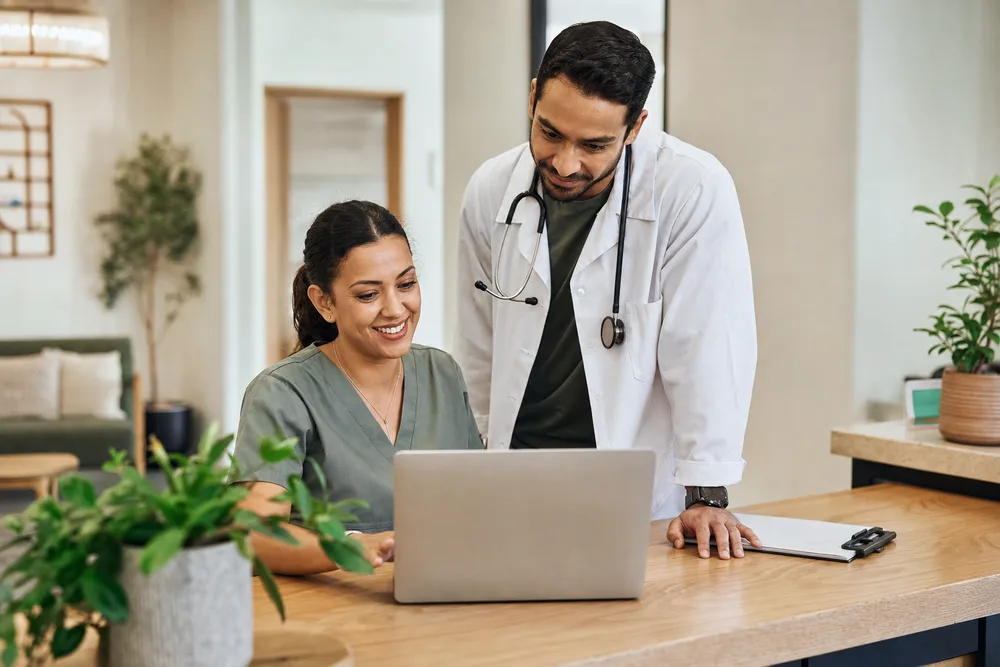 A practice manager and physician reviewing work together at the front desk